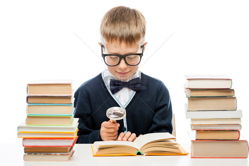 有眼镜的聪明男孩用放大镜正在考虑这本书的文本图片