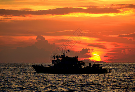 太阳背景下海中渔船的剪影图片