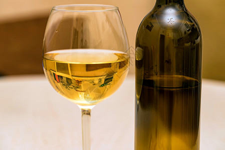 瓶子和白葡萄酒的特写镜头倒入玻璃杯中图片