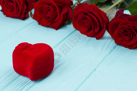 红玫瑰和心形盒新鲜玫瑰和蓝木本底的红天鹅绒珠宝盒情图片