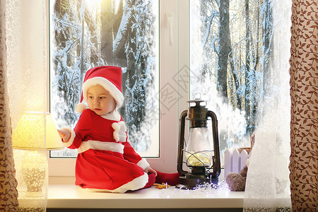 一个过年的孩子望着窗外孩子们正在等待圣诞老人一个穿着圣诞套装的图片