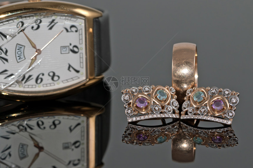 妇女金耳环与宝石的对等配金耳环和在用玻璃打碎的优雅手表背景反射表图片