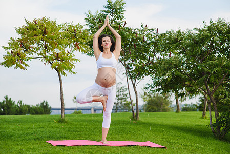 美丽的年轻孕妇站在Vrksasana运动中做瑜伽图片