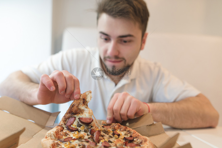 一个脸饥肠辘的帅哥从盒子里收紧了一块披萨图片