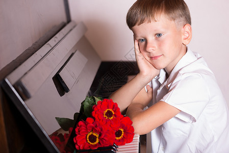 一位年轻的钢琴家拿着一束红花坐在钢琴前古典音乐的独奏会安表演结束后图片