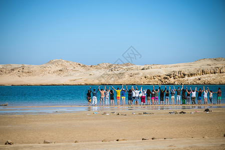 一群人手牵站在一片被沙漠包围的蓝色湖边上他图片