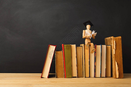 戴着毕业帽的木制偶坐在旧书上高清图片