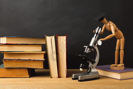 戴着毕业帽的木制偶站在显微镜下看着书堆高清图片