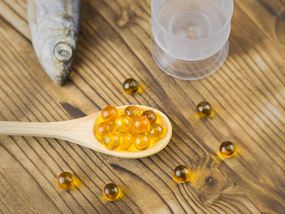 餐桌上的木勺子鱼油药片和背景中的鱼治疗自然成分传统医学这图片