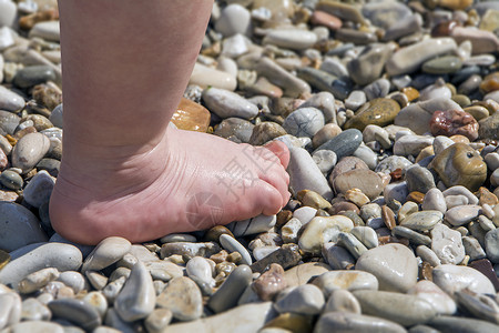 儿童脚的缝合在沙滩上的小石头上图片