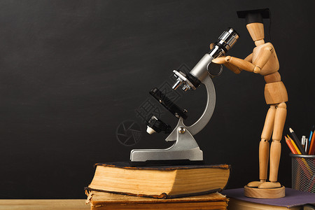 在毕业帽子中的伍德木马丽昂尼特在显微镜中看着空教室黑板图片
