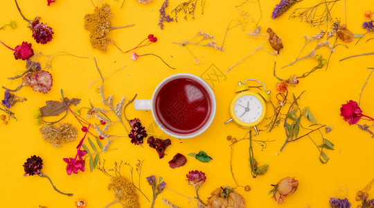 一杯红茶小闹钟和草药黄色背景图片