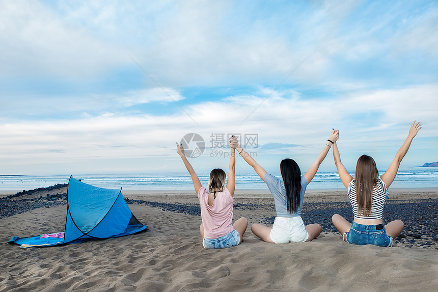 三名年轻女背影是举起手来在海岸线图片