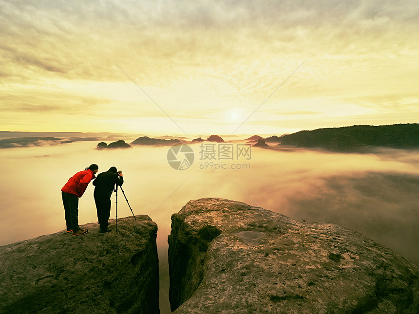 两个男人喜欢在野外拍照自然摄影师用三脚架上的大相机留在山顶岩石上听缪斯唤图片