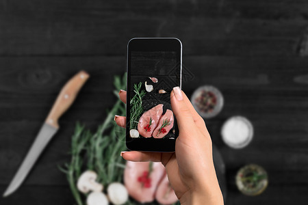 手持智能手机的女在黑色背景下制作了生鸡胸照片图片