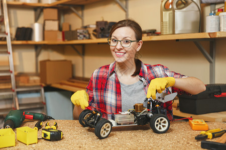 穿着格子衬衫灰色T恤黄色手套制作玩具车铁模型构造器的年轻女子背景图片