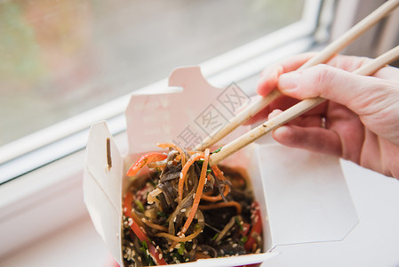 外卖盒和筷子双手用筷子从盒子里拿出亚洲食物外卖盒里有蔬菜的面条图片