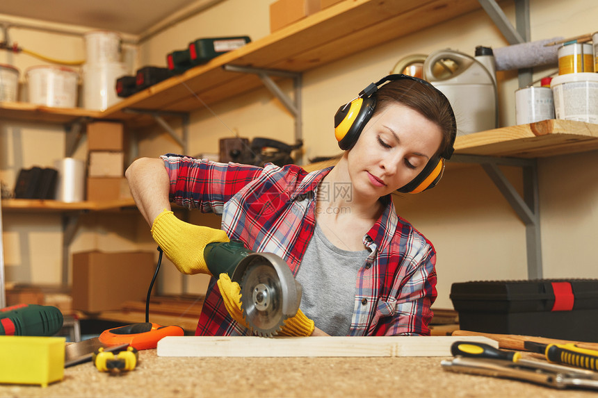 身着格子衬衫灰色T恤隔音耳机在木工车间用不同工具作的黄色手套用电锯木头的棕色图片