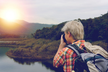 旅行者背着包在山和湖旅行旅游背包客使用相机拍照生活方图片