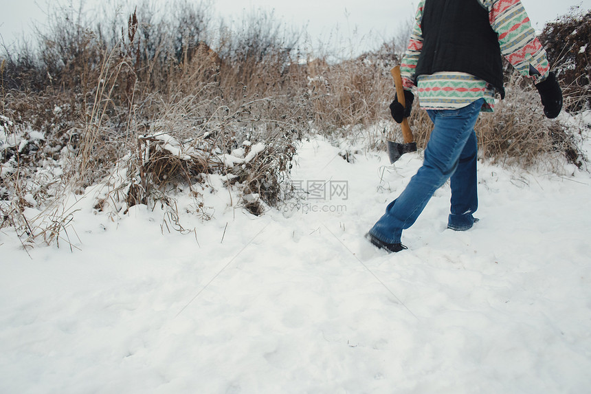 一个手拿着斧子的男人在雪路上行走开图片