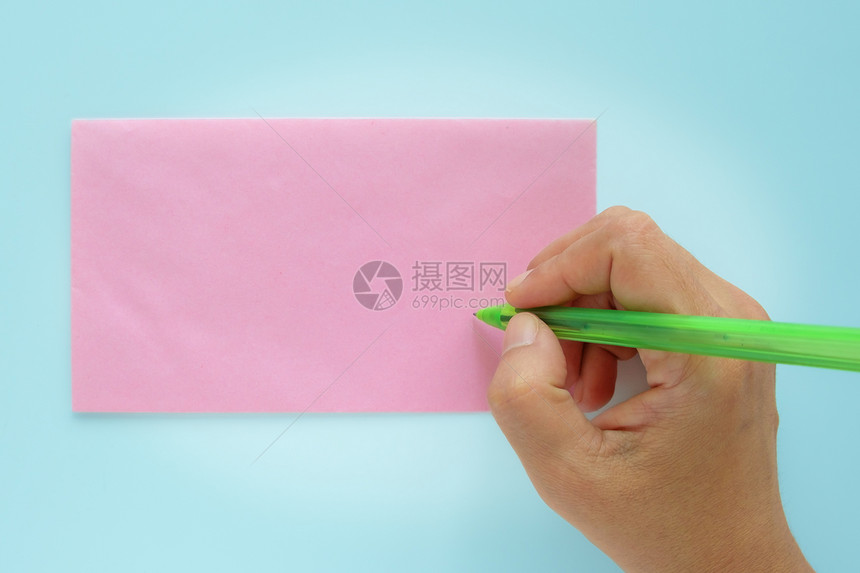 手在蓝色背景的粉红色信封上被寻址图片