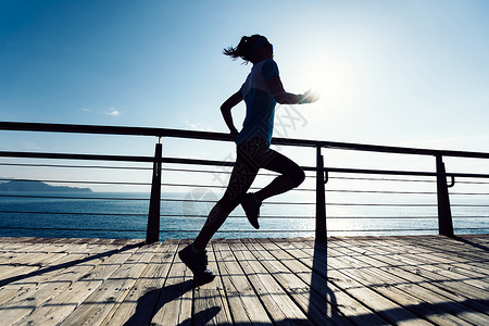 防水防汗日出时在海边木板路上奔跑的健身女跑者背景