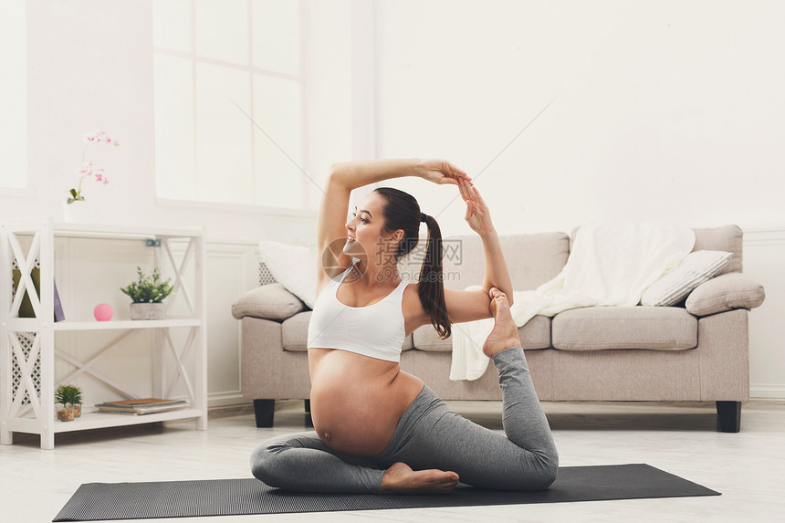 快乐的孕妇在家中以骆驼姿势训练瑜伽母积极怀孕幸福训图片