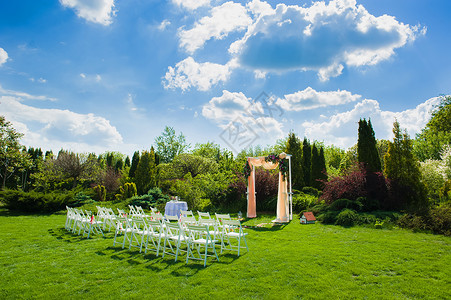 在美丽的婚礼拱门前的白椅子上面有自然背景图片
