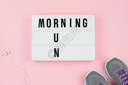 粉红色背景上的灯箱耳机和运动鞋上的晨跑文本励志名言图片