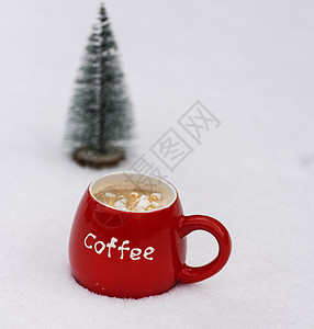 白色雪地上放着咖啡和棉花糖的红色陶瓷杯图片