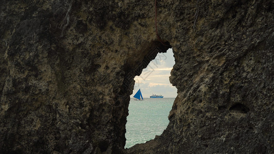 帆船通过岩石上的一个洞查看有蓝色风帆的船游艇在海洋中海上的帆船菲律宾图片