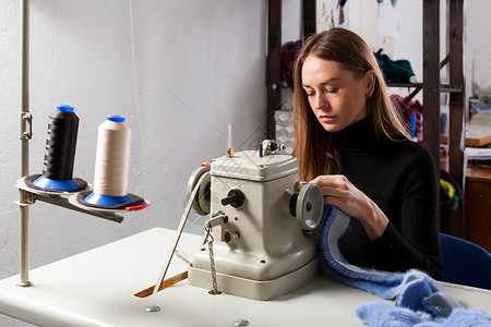 在车间缝纫机上缝制蓝色毛皮大衣的年轻女子皮毛商图片