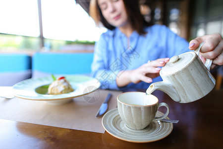 漂亮的女孩从茶壶里把茶倒进杯子里图片