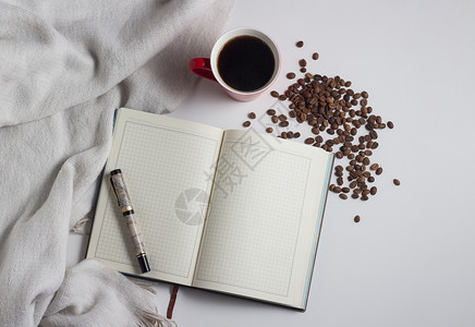 白色围巾日记钢笔红杯咖啡和白色背景上的咖啡粒图片