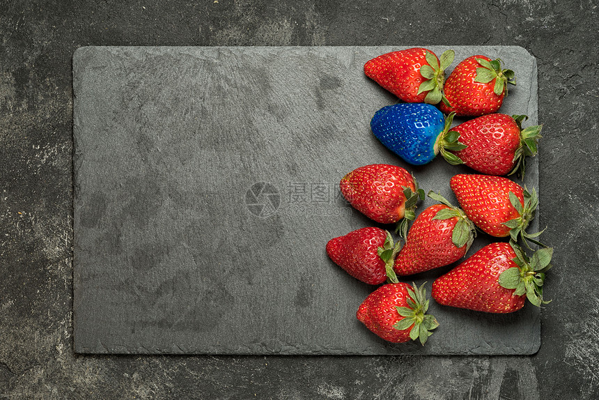 个排他更好的选择的概念黑色石盘背景上的红色草莓中的一个蓝色草莓带有复制图片