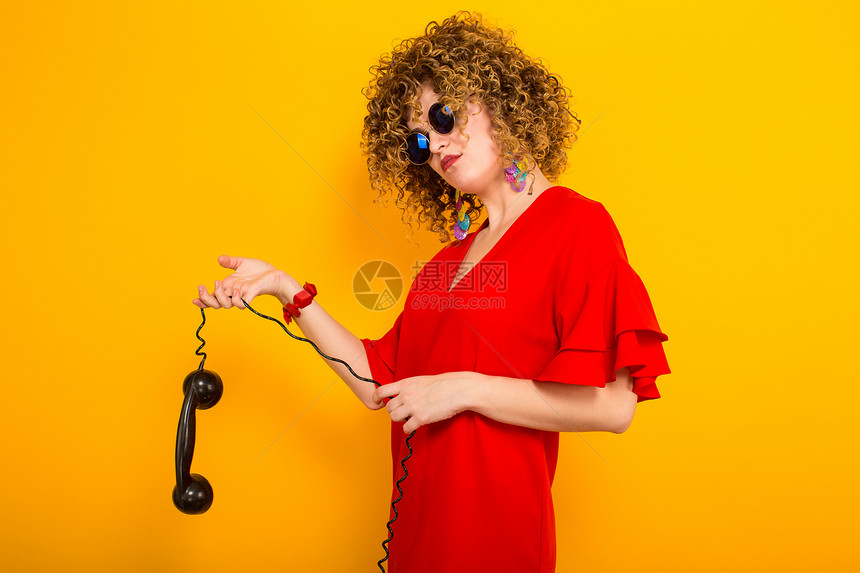 穿着红礼服和墨镜的年轻卷发美女拿着旧电话手图片