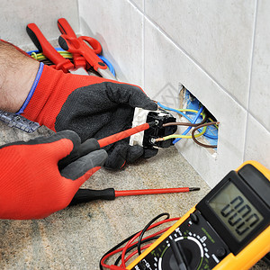 配有手套和安全仪器的电工技师将电缆固定在一个住宅设施的套座上图片