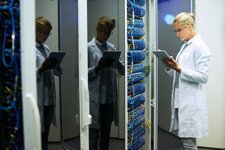 身穿实验室大衣的年轻美女与超级计算机将数据输入到数字平板电脑图片