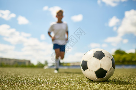 无法辨认的少年男孩在足球练习中田野踢球时图片