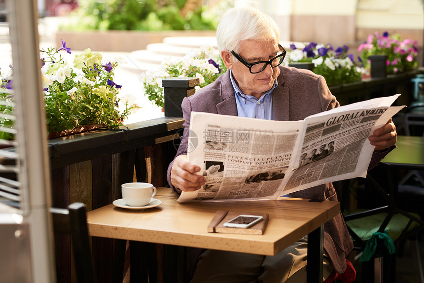 在户外咖啡馆阅读晨报的长者图片