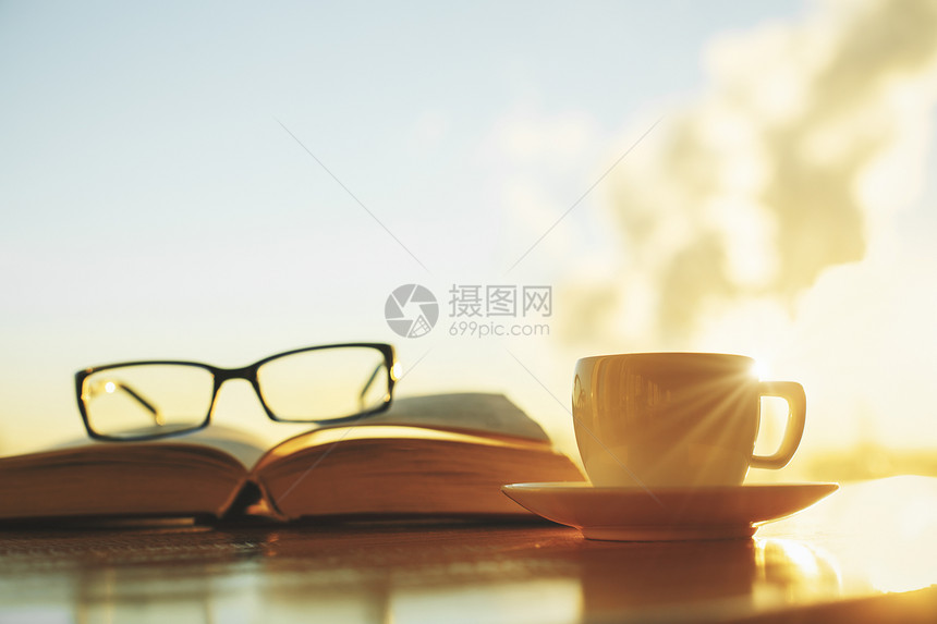 在模糊的天空背景上贴近书籍眼镜和咖啡杯图片