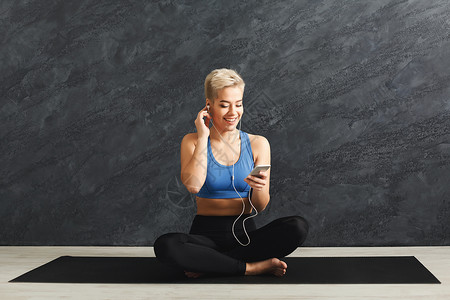 快乐的健身女人休息和听音乐年轻的女孩坐在耳机的垫子上健美健康的图片