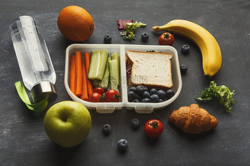 健康食品的概念午餐盒装满了混合蔬菜三明治蓝莓黑桌背景上的水图片