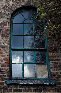 一栋废弃建筑的砖墙上有一扇古老的深绿色拱形窗户图片