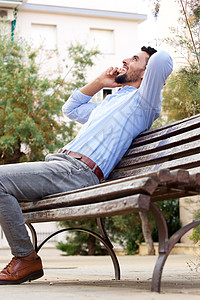 年轻人坐在长椅上在用手机交谈时微笑图片
