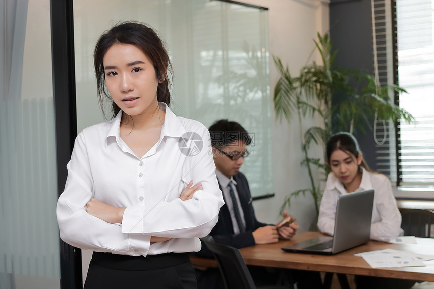 充满自信的亚洲年轻商业妇女与会议室背景的同事站在办公室里图片