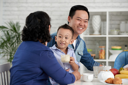 微笑的亚洲父亲和小男孩在与大家庭共餐桌前图片