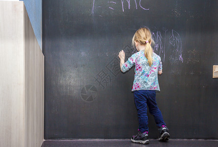 可爱的小女孩在教室的黑板上写字图片