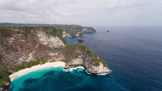 悬崖脚下的野生热带海滩在岩石峭壁之间的热带海滩印度尼西亚巴厘岛努沙佩尼达岛上的KarangDawa曼塔湾或Kelingking海背景图片
