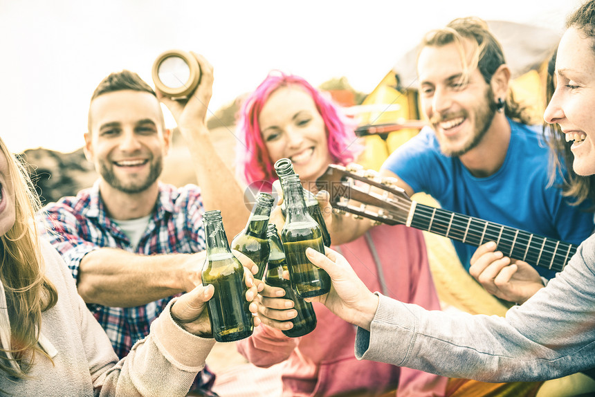 年轻朋友在海滩露营派对上玩得开心友谊旅行概念与时髦的人流浪者在夏季冲浪营弹吉他和喝瓶装啤酒温暖图片